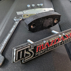 Emblem "Mazdaspeed" für den Kühlergrill; gibt es in der Bucht. Zusätzlich selbstgebauter Lückenfüller aus einer Siebdruckplatte passgenau für "in die Raute" (schwarz), ein Alublech mit etwas größer als die Raute, Befestigungsplatte, Schrauben.